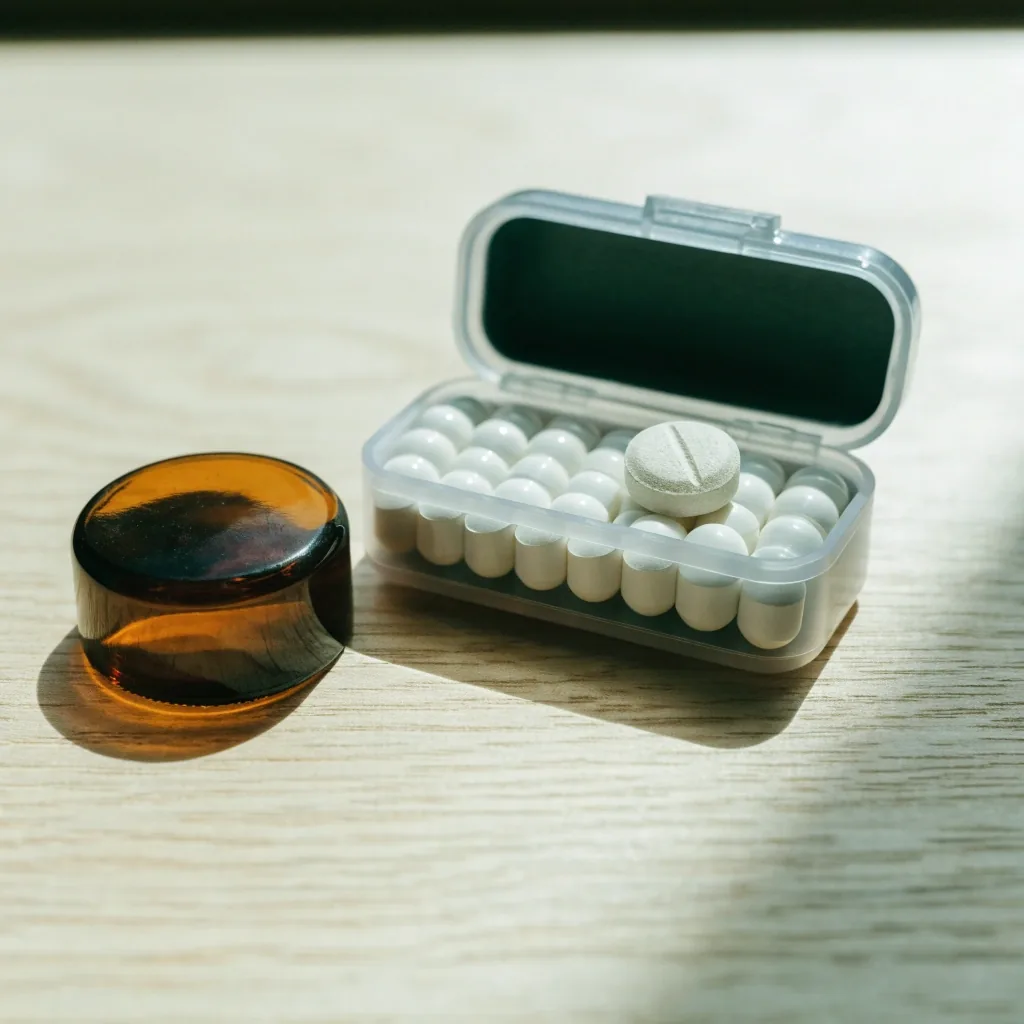 A small open travel case with a neat row of unlabelled capsules and a tablet beside a bottle cap